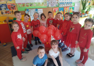 Dzieci pozują do zdjęcia ustawione przy koszu z czerwonymi balonami